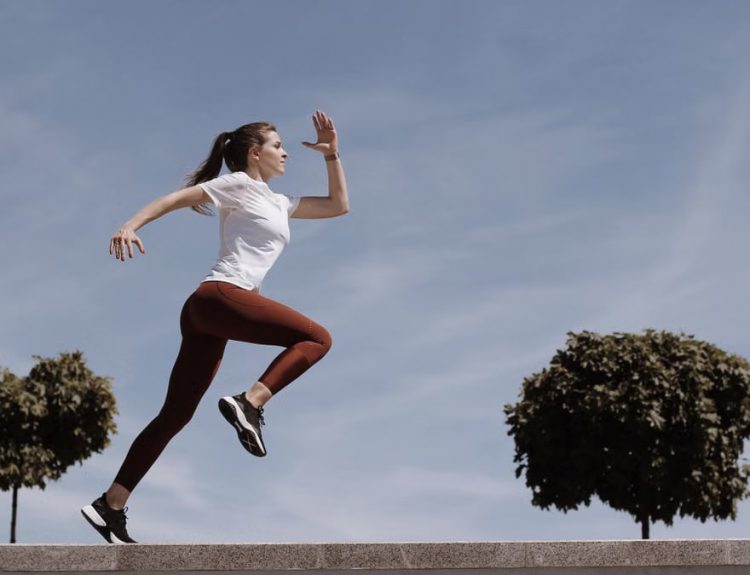 Athletic woman running on an outdoor road, demonstrating fitness and determination under a blue sky.