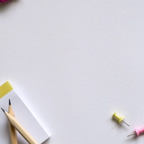 Flat lay of desk items including a planner, pencils, erasers, and push pins on a white background.