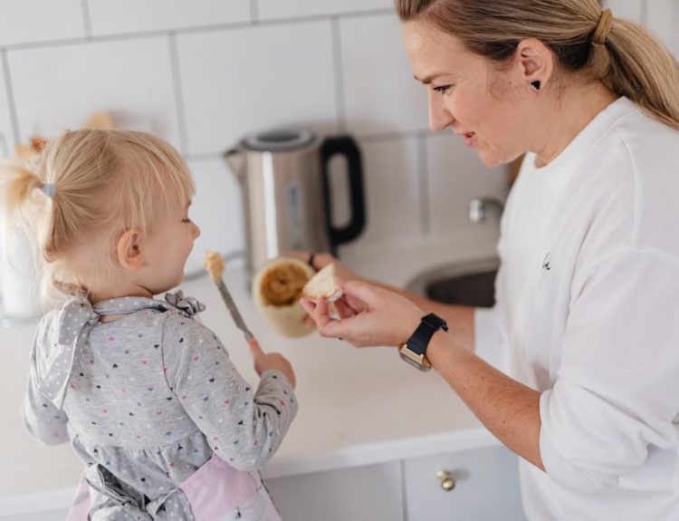 A mother and her young daughter interact while preparing food in a modern kitchen.
